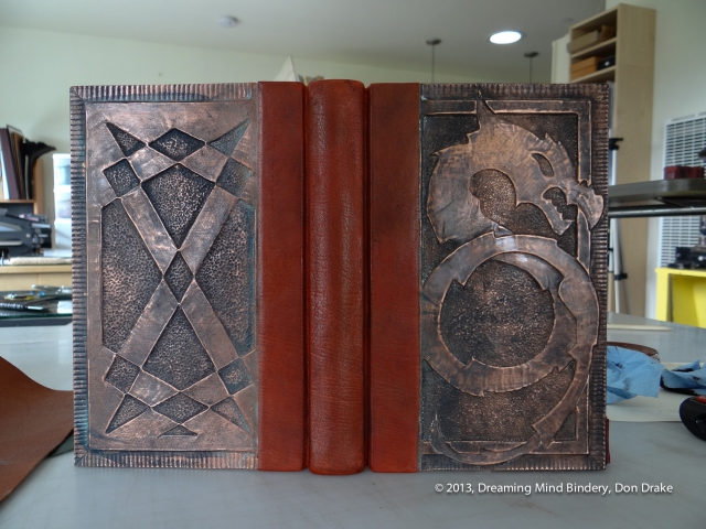 A quarter bound, leather and copper journal with a dragon design on the front cover and a geometric design on the back cover. The copper has a dark, almost black patina created with vinegar and salt.