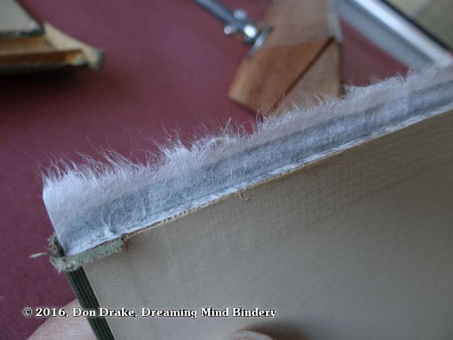 A detail of the inside, spine edge of a cover board that has become detached from the book spine and which has had a kozo guard attached in preparation of repair of the joint
