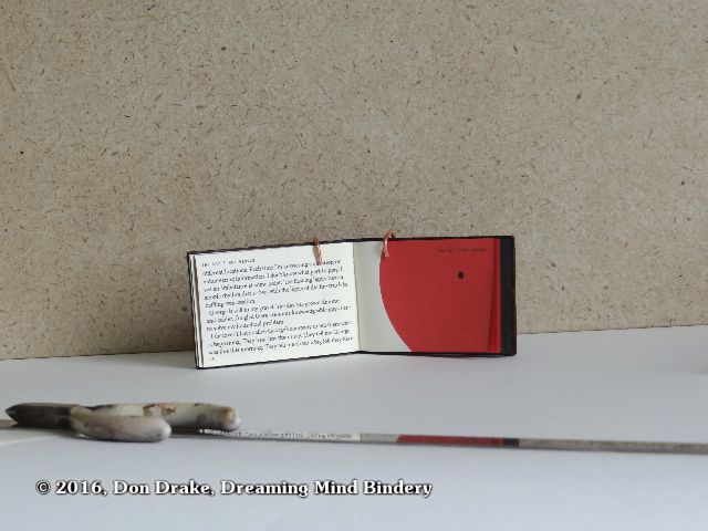 A miniature book being held open with a wire bracket to allow photographing its interior