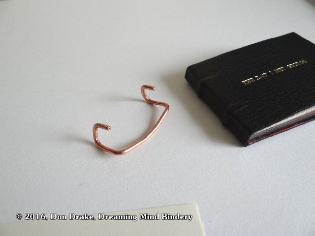 A wire bracket to hold a book open for display and photography