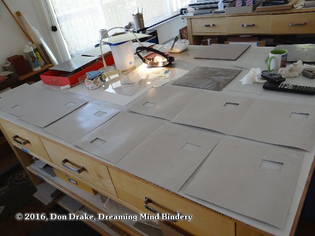 Chipboard layers of laminated book covers after the priming adhesive has started to dry and the moisture migration has stabilized