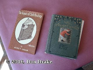 A first American edition of 'The Secret Garden' in need of repair and a copy of The Repair of Cloth Bindings (Arthur W. Johnson) on a bench top